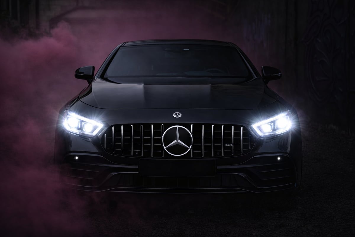 Black Mercedes-AMG sports car front view with illuminated LED headlights against a dark purple smoky background